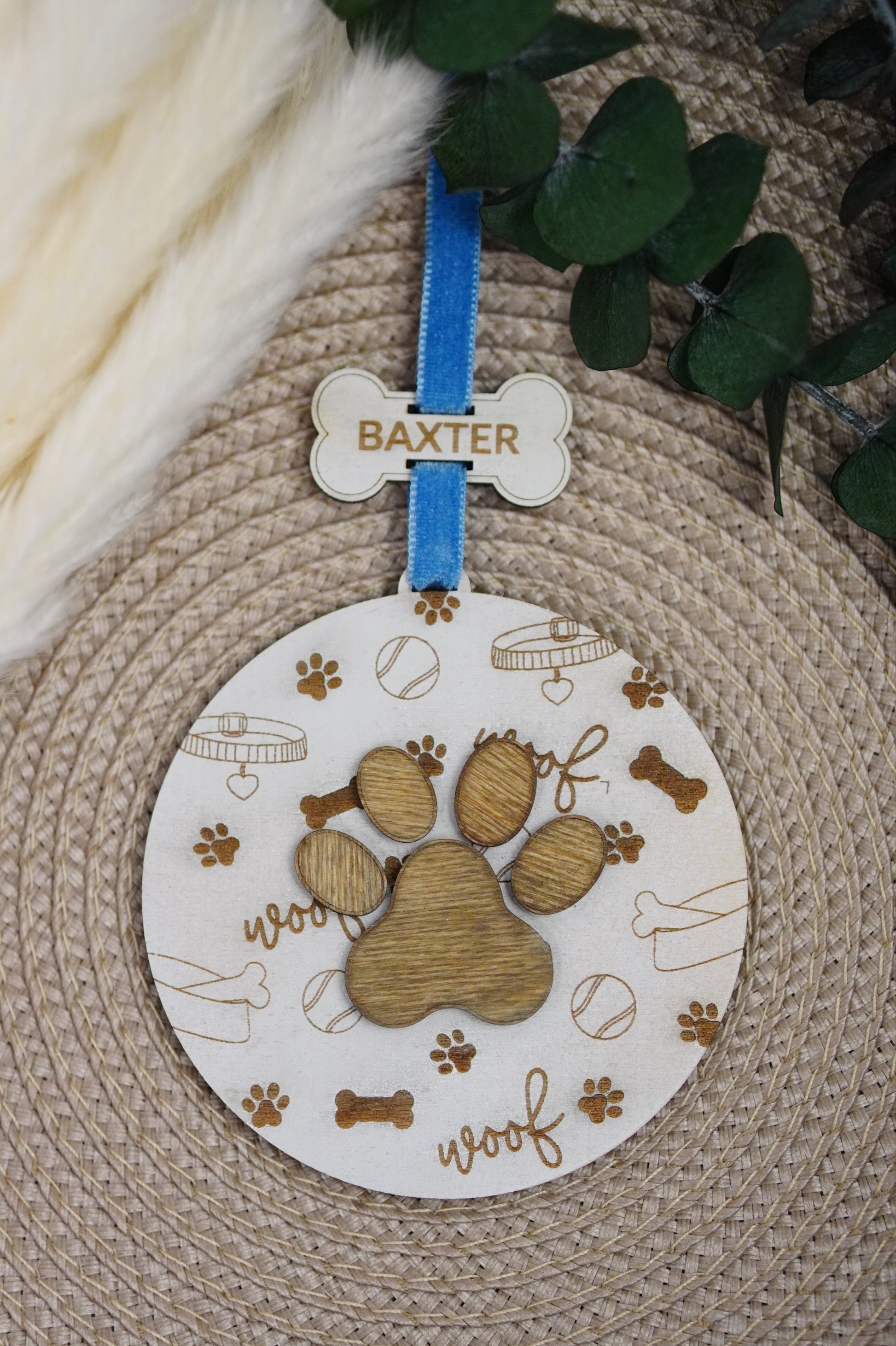 Wooden paw print design with a blue ribbon and 'Baxter' tag on a textured surface.